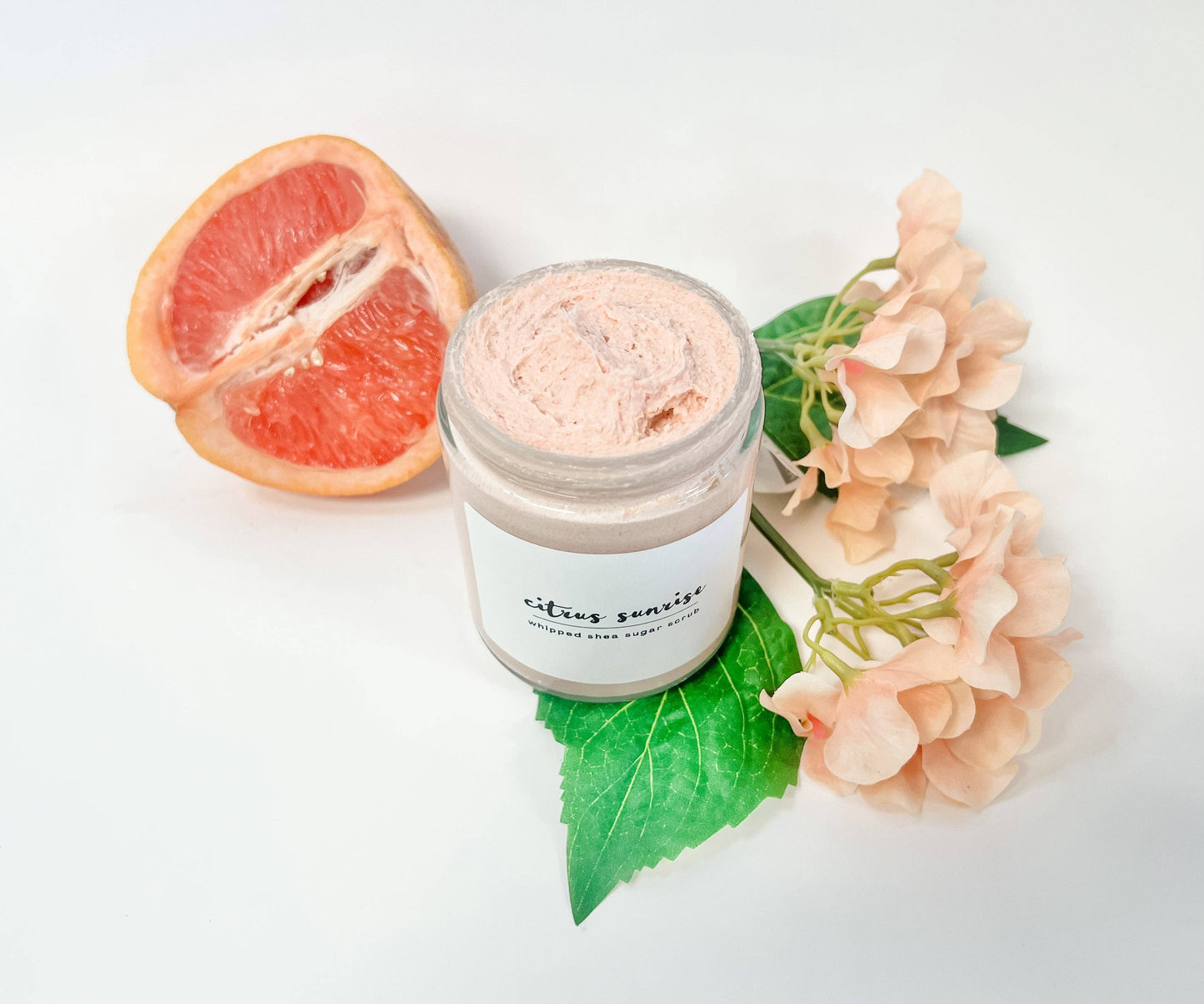 Jar of citrus scented body sugar scrub with an orange and flowers on a white background
