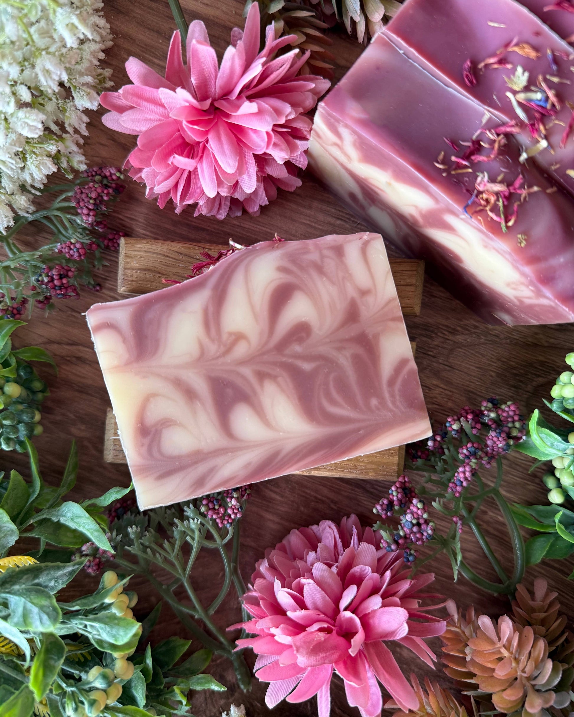 Two swirled soap bars on a wooden surface with pink flowers and greenery.