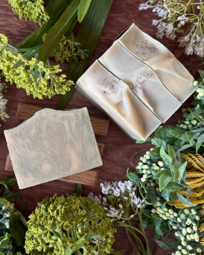 Three green bars of soap on a wooden surface with greenery around