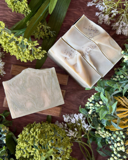 Three green bars of soap on a wooden surface with greenery around