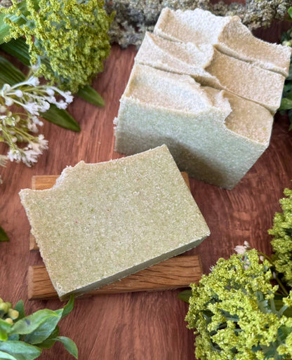 4 Green soap bars. one soap bar is layed on a wooden surface with flowers in the background