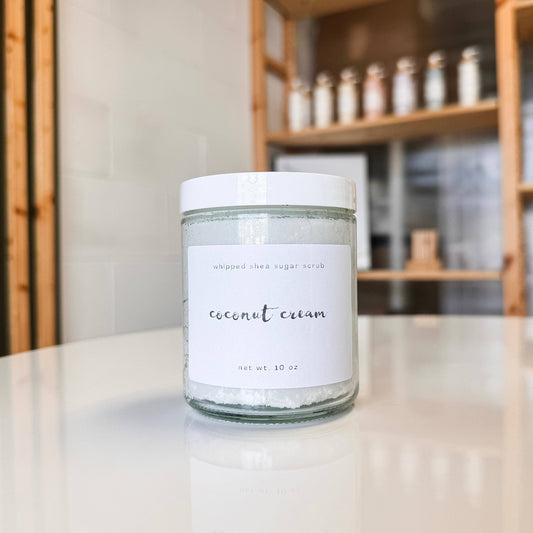 Jar of coconut cream sugar scrub on a table with shelves in the background