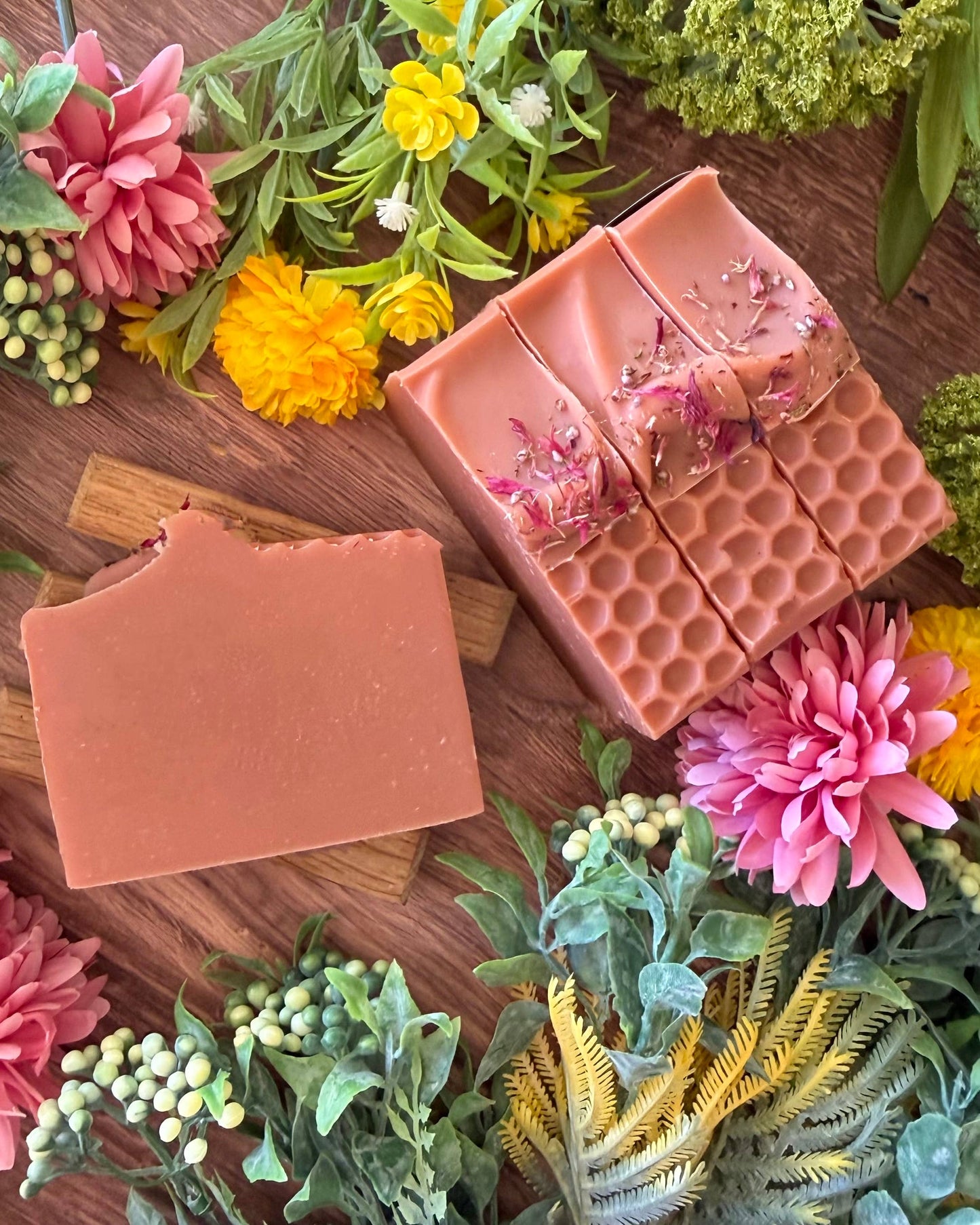 Pink soap bars with floral elements on a wooden surface with flowers and plants.