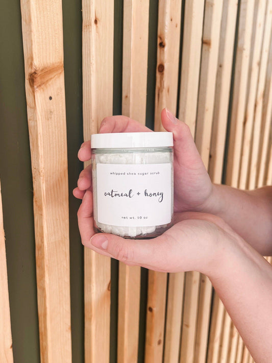 Hand holding a jar labeled 'oatmeal + honey' against a wooden background