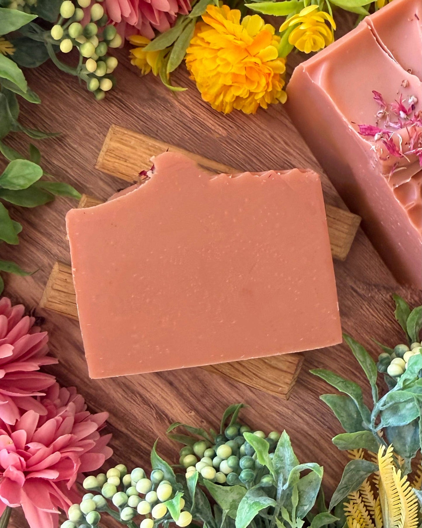 Pink bar of soap on a wooden board with flowers around