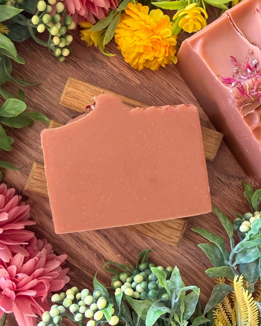 Pink bar of soap on a wooden board with flowers around