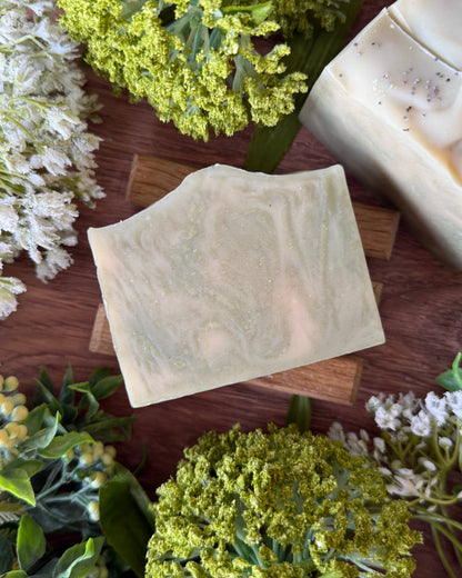 Bar of green soap on a wooden surface with greenery