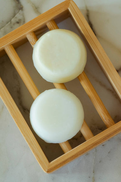 Wooden bamboo soap holder holding two small round white soaps. 