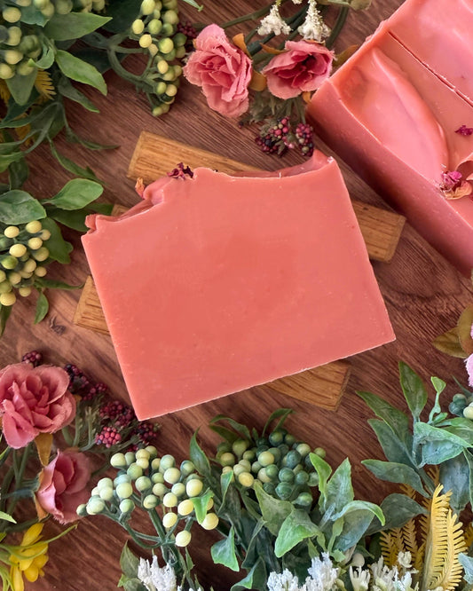 Pink soap bar on a wooden surface with flowers and greenery