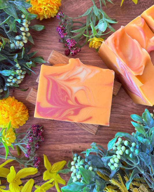 Two swirled soap bars on a wooden surface with flowers and greenery around.