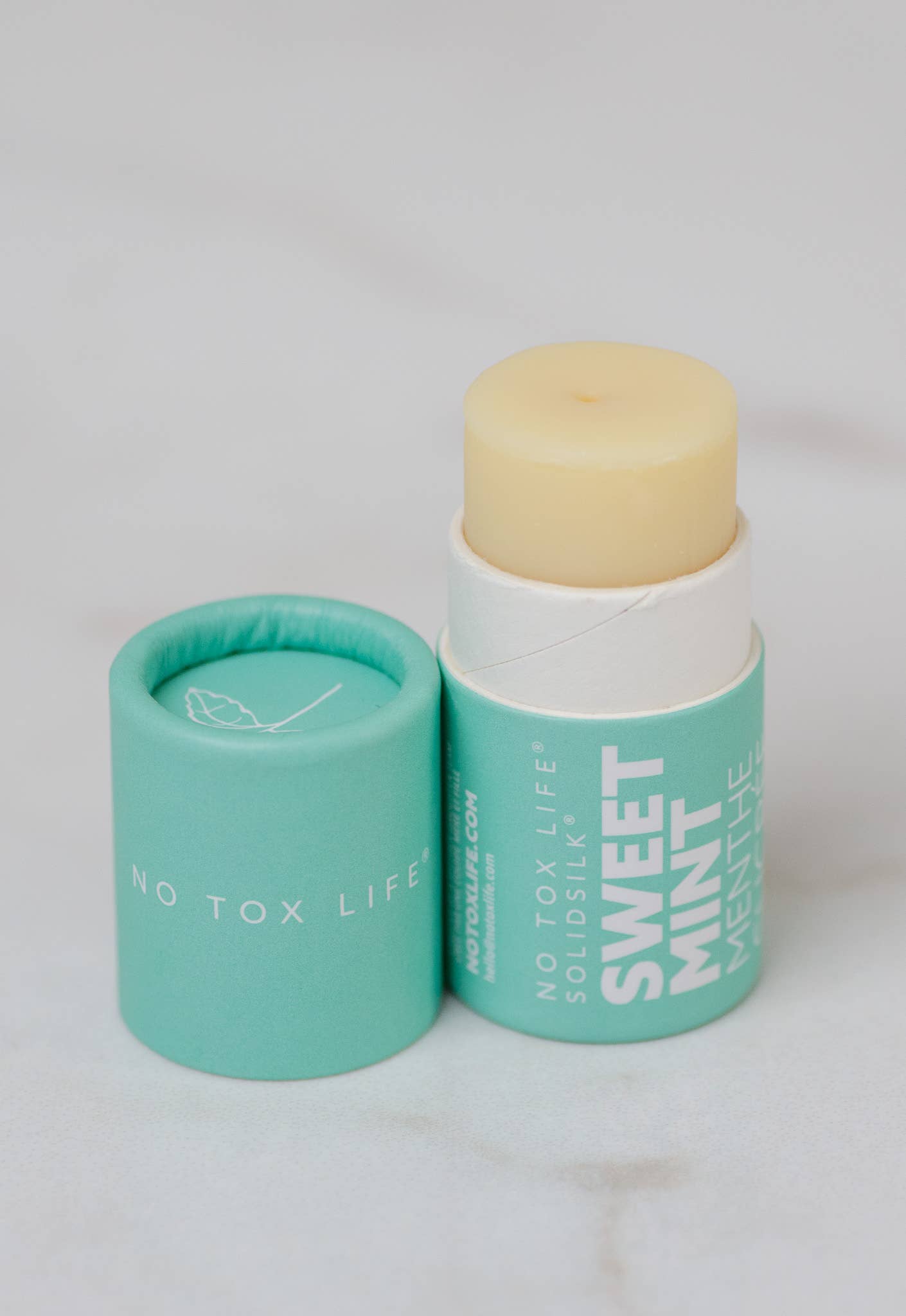 Balm with a green container labeled 'No Tox Life' on a light gray background