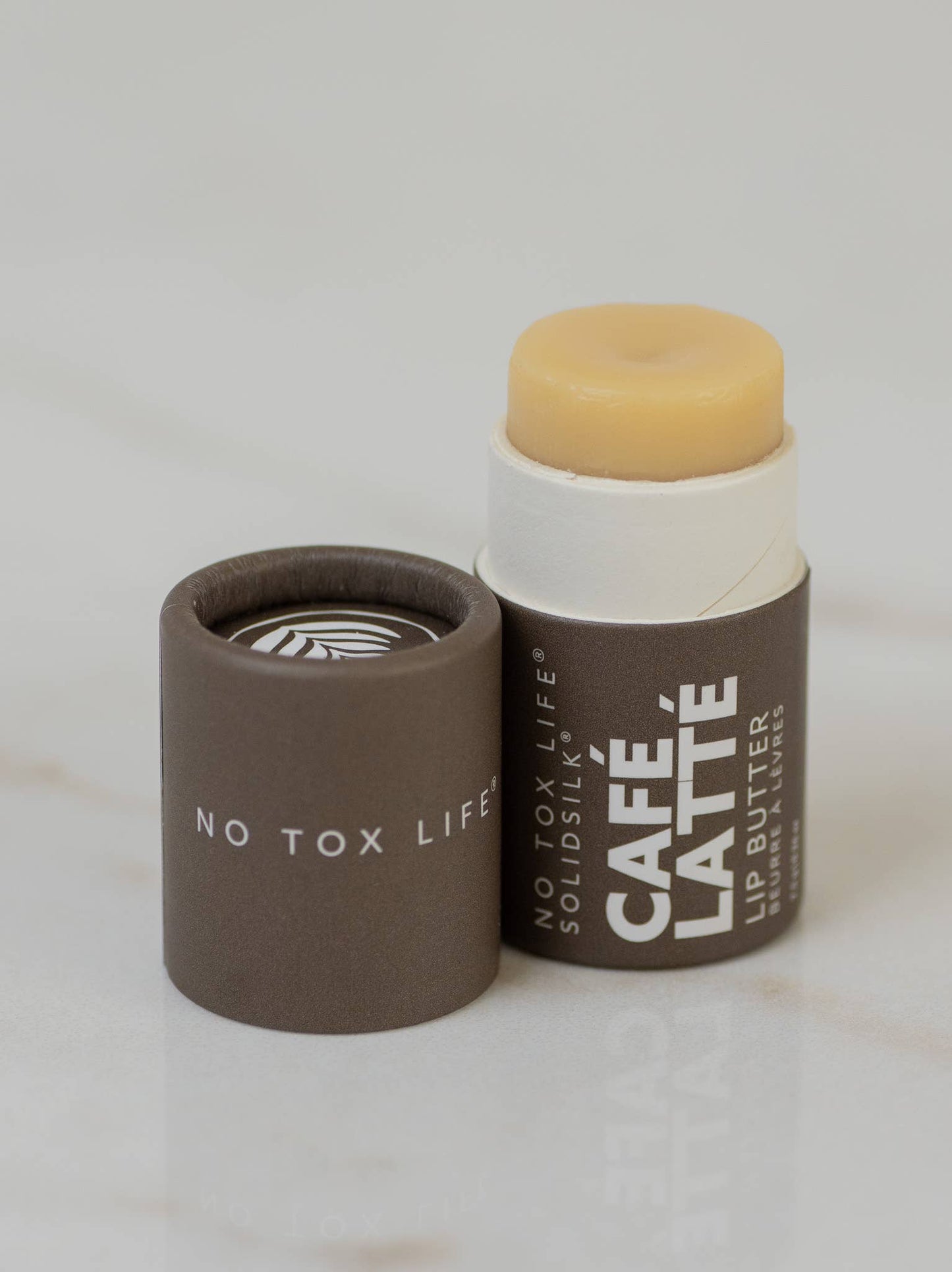 Lip butter stick with brown container and 'Café Latè' branding on a light gray background
