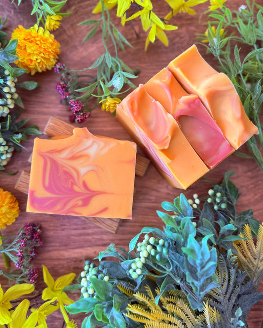Two soap bars with a marbled design on a wooden surface surrounded by flowers and greenery.