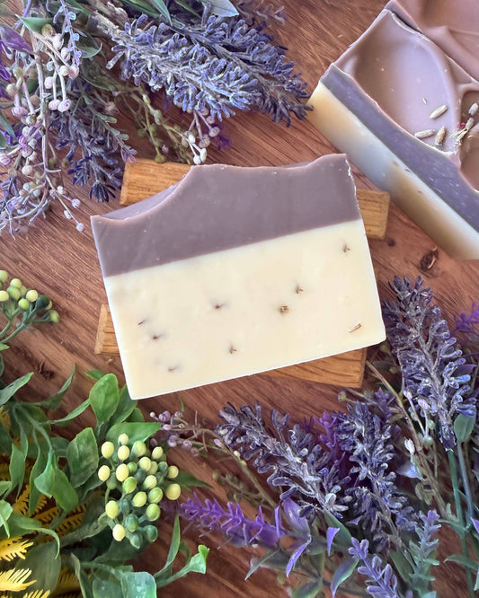 Two bars of soap on a wooden surface with lavender flowers and greenery.