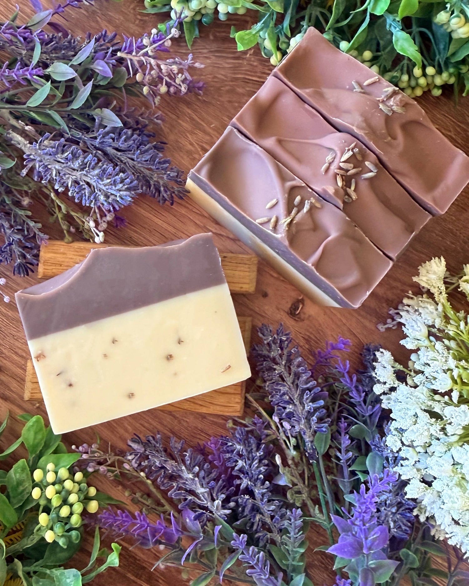 Three soap bars on a wooden surface with lavender and other flowers around