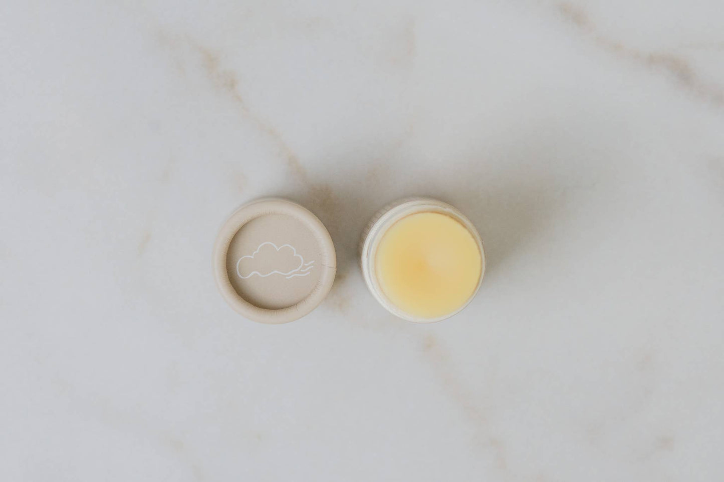 Two small round containers with beige lids on a marble surface