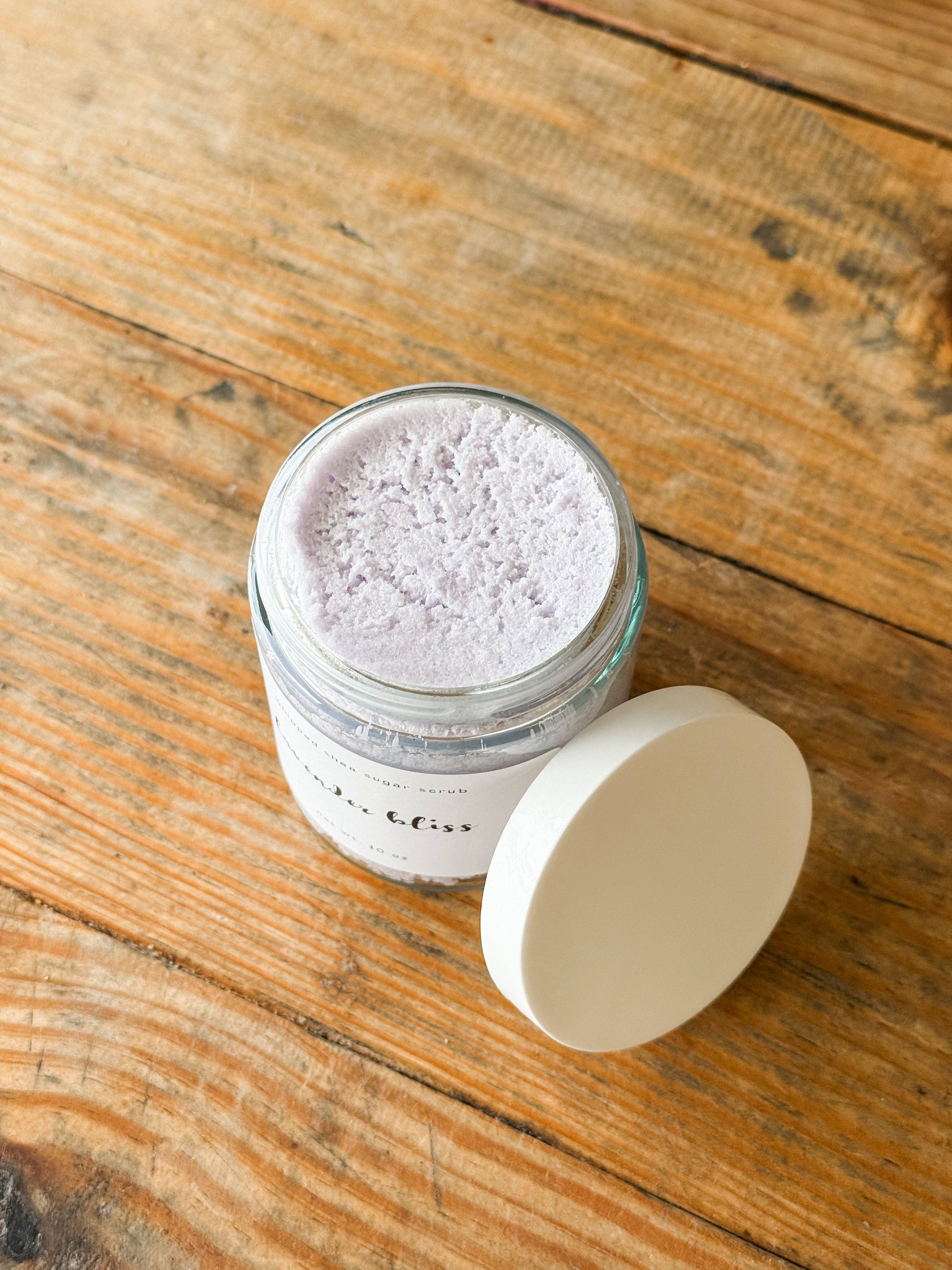 Jar of sugar scrub on a wooden surface with lid layed on side. 