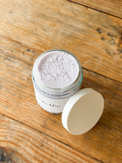 Jar of sugar scrub on a wooden surface with lid layed on side. 