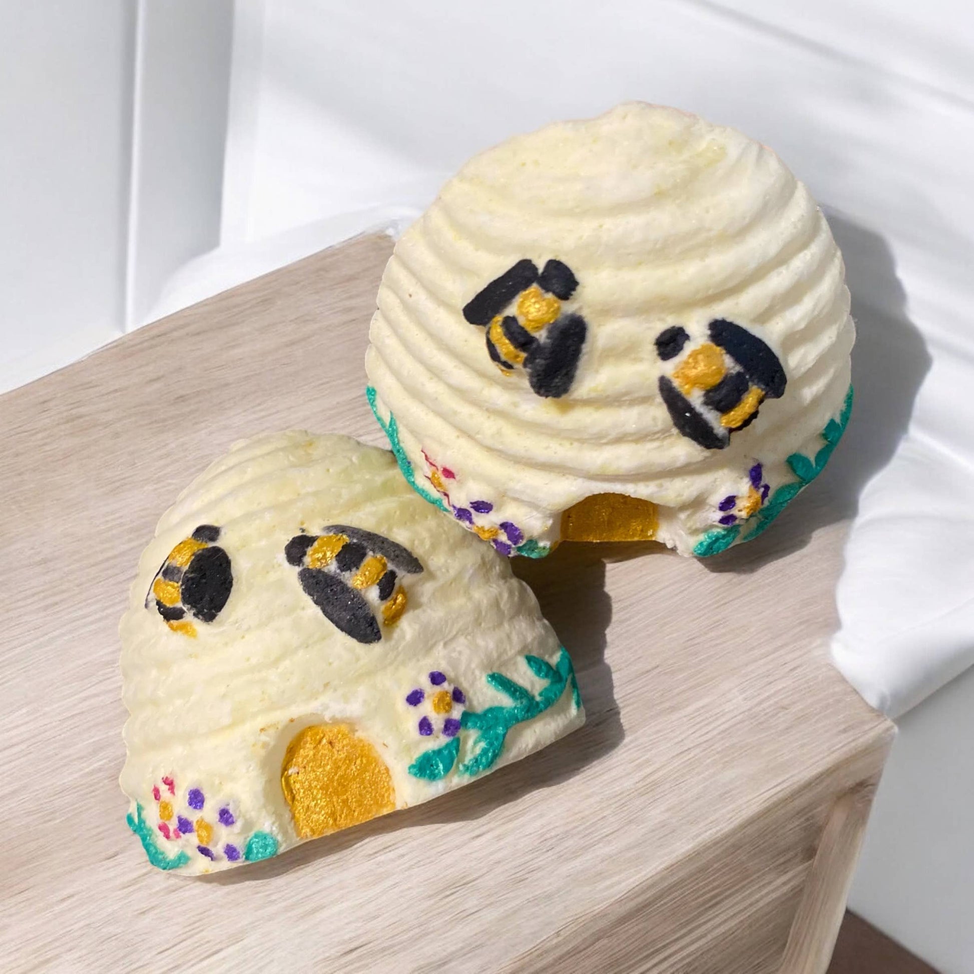 Two bee-themed bath bombs on a wooden surface with a white background