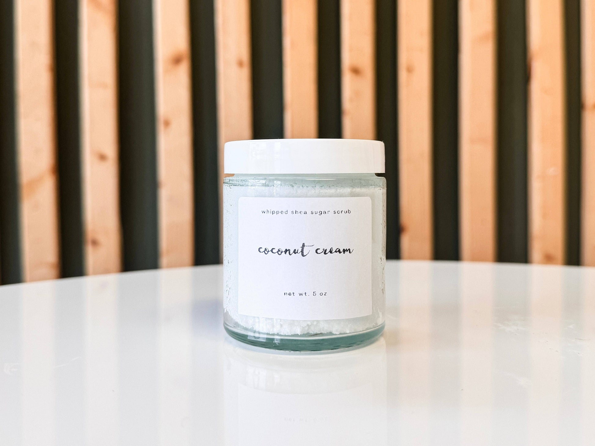 Jar of coconut cream sugar scrub on a white surface with a wooden background